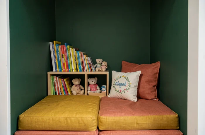 Coin lecture bébé en alcôve avec coussins en lin moutarde et terracotta, bibliothèque basse en bois et coussin personnalisé brodé avec le prénom